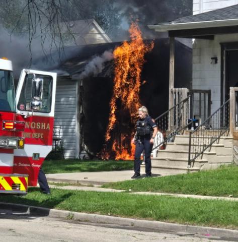 Firefighters arrive at a garage fire as a police officer tries to roust any occupants from a nearby house. 