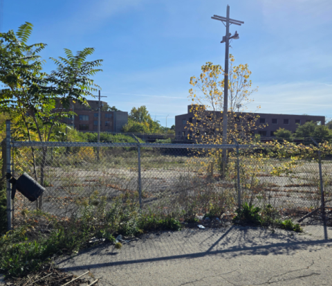 Photo of a largely vacant lot with a partially-demolished building in the background. 