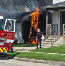 Firefighters arrive at a garage fire as a police officer tries to roust any occupants from a nearby house. 