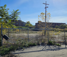 Photo of a largely vacant lot with a partially-demolished building in the background. 